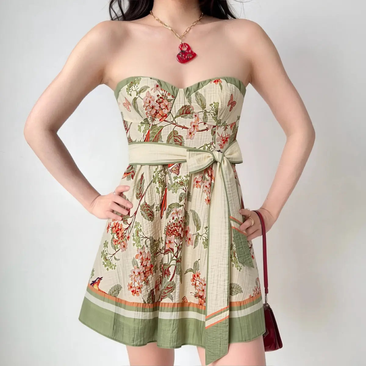 Indoor lifestyle shot of retro floral bird butterfly print strapless mini sundress, textured linen fabric, wide matching waist sash big side bow, green striped hem trim, sweet countryside vacation dating outfit.