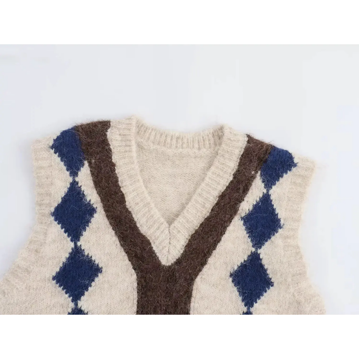 Cream fuzzy knit vest close-up, v-neck with brown Y shape trim and navy blue argyle diamond pattern