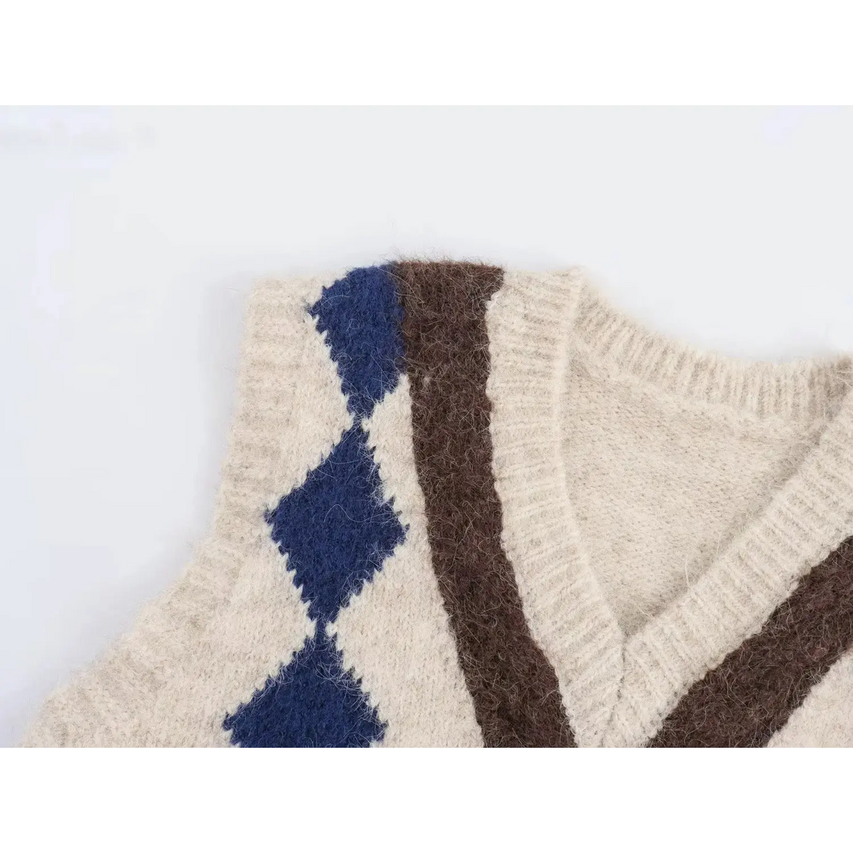 Close-up of shoulder part of cream fuzzy knit vest, navy blue argyle diamond and brown jacquard pattern