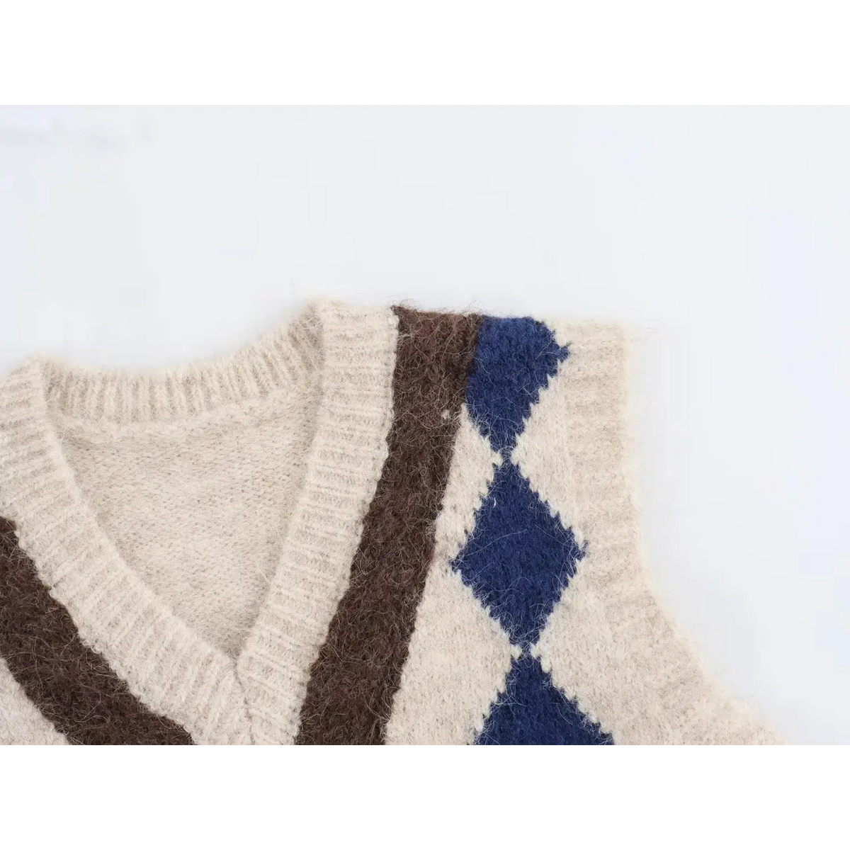 Macro shot of V-neck and shoulder area, cream fuzzy knit with brown Y trim and navy diamond argyle print
