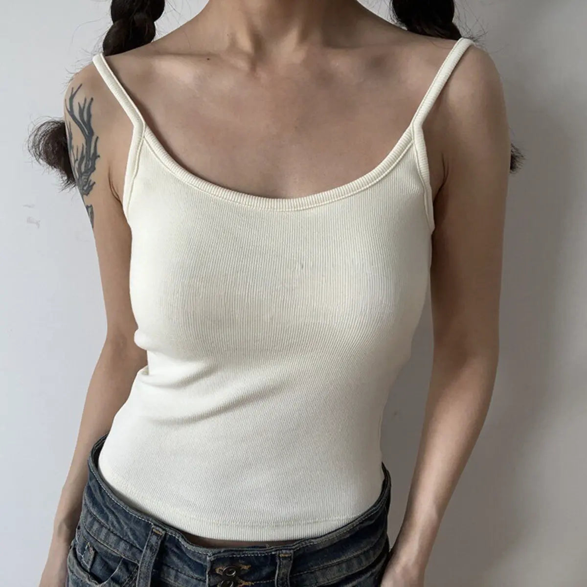 Lifestyle shot of form-fitting cream beige ribbed camisole with thin straps, tucked into jeans