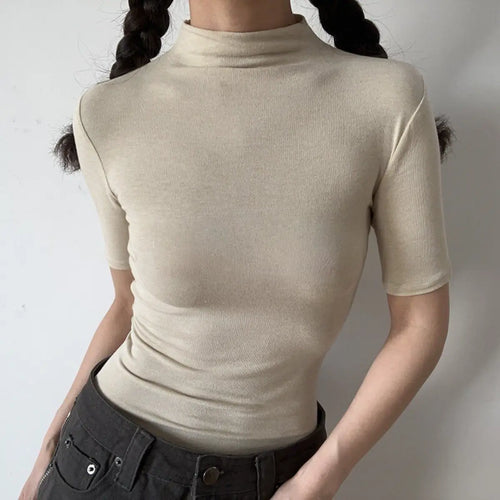 Lifestyle shot of form-fitting cream beige ribbed half-turtleneck short-sleeve top, tucked into jeans