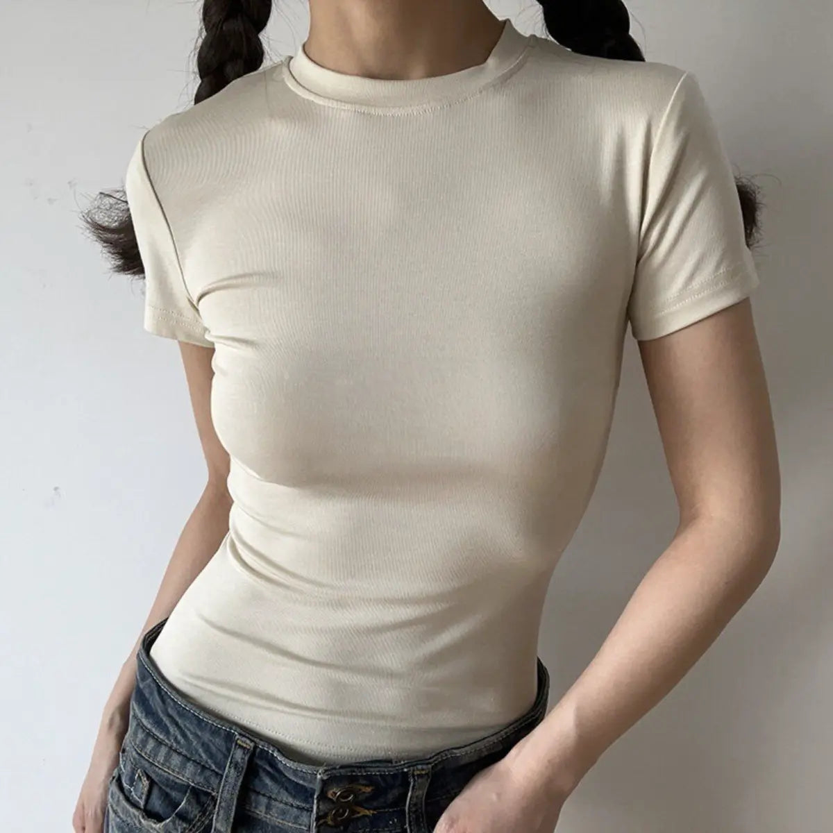 Lifestyle shot of form-fitting cream beige ribbed crew-neck t-shirt, tucked into jeans