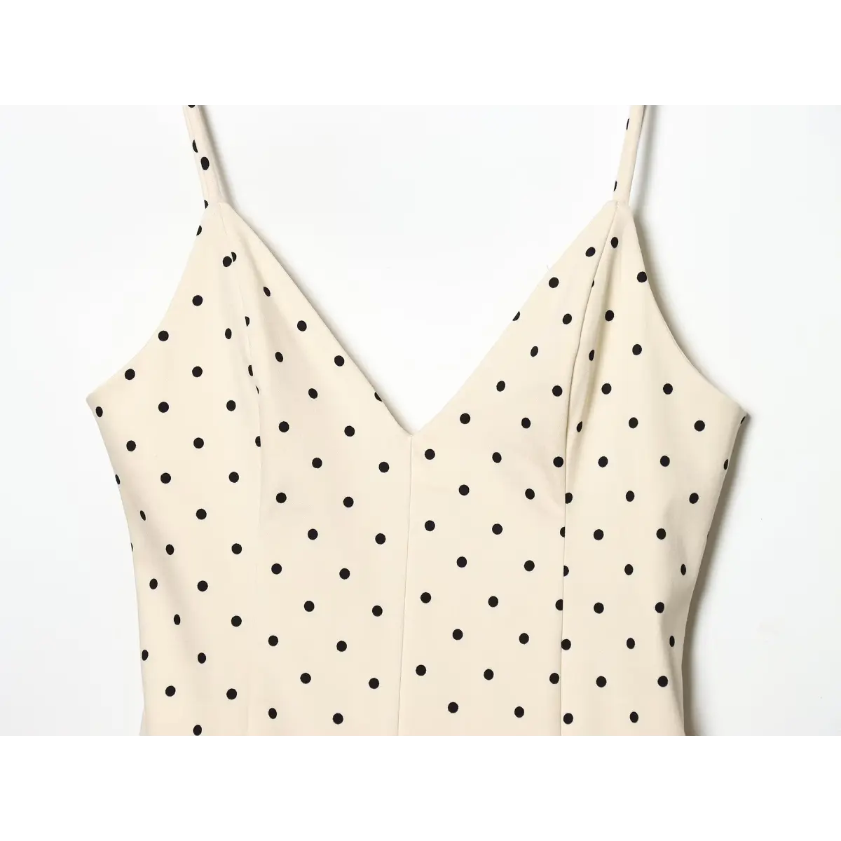 Upper bust close-up of off-white black polka dot slip dress, deep V-neck with vertical princess seam tailored bodice.