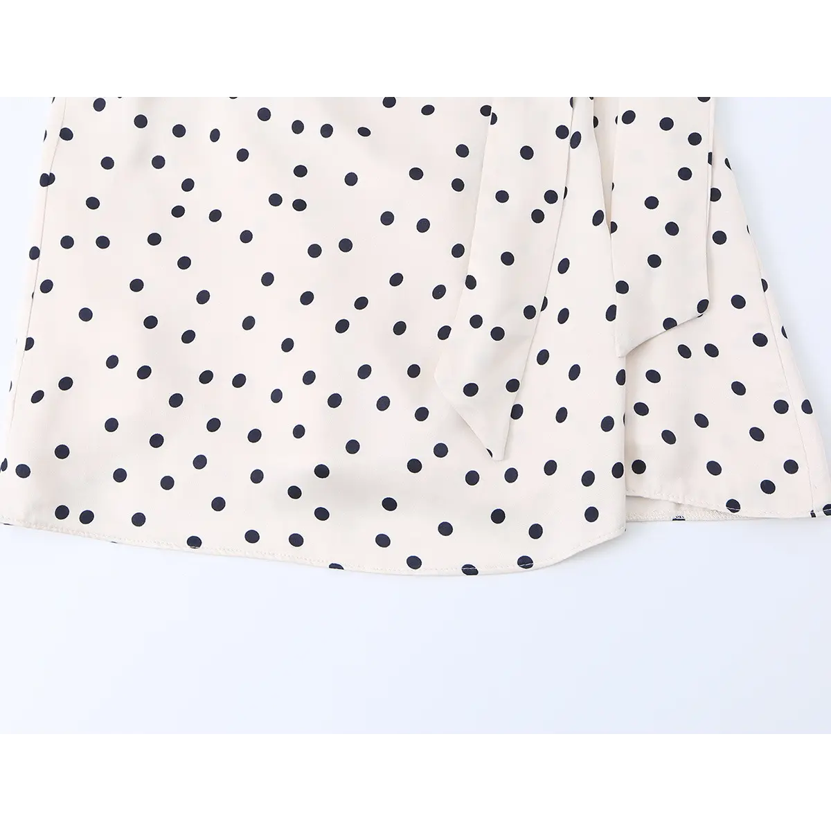 Close-up of the dress's wrap skirt, showing the cream and black polka dot print and the self-tie closure.
