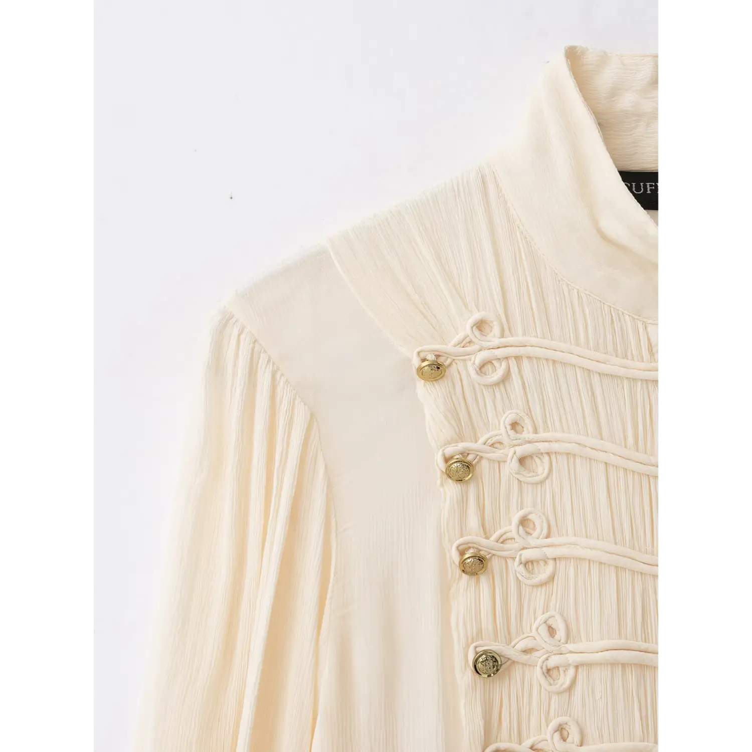 Close‑up of shoulder and front frog knot buttons with gold metal studs on cream blouse