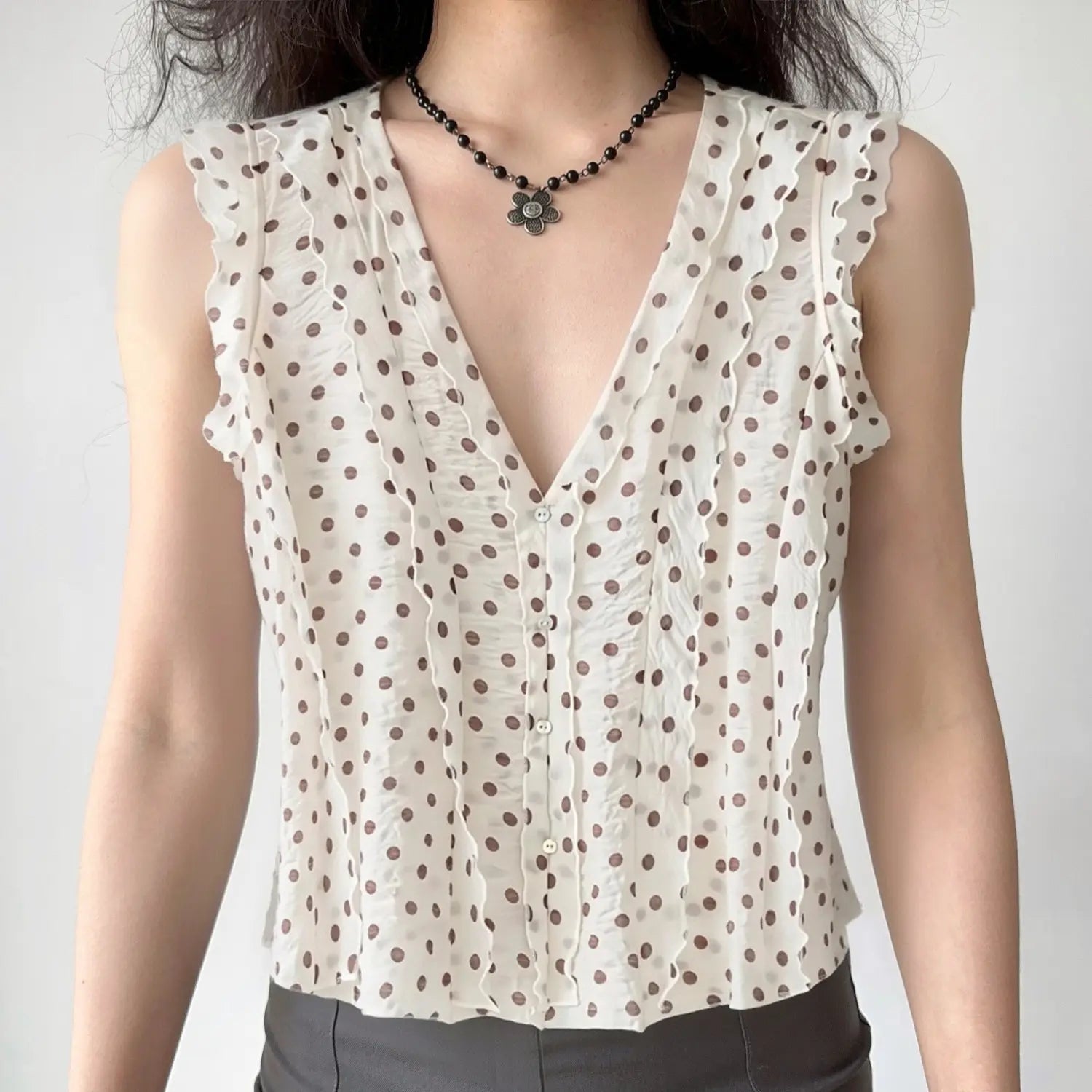 Front lifestyle shot on model of cream brown polka dot sleeveless blouse, deep v neck wavy frill trim, vintage casual summer outfit