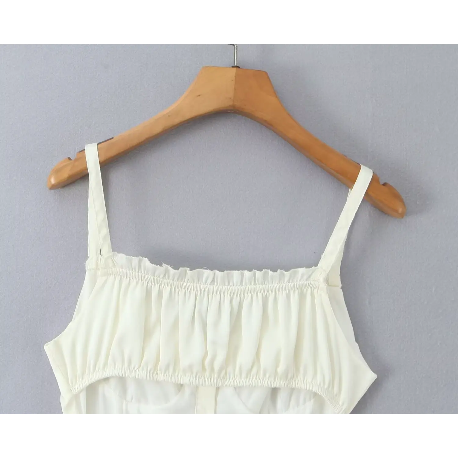 Close‑up upper back ruffle elasticated gathered neckline cream cami mini dress hanging on wooden hanger