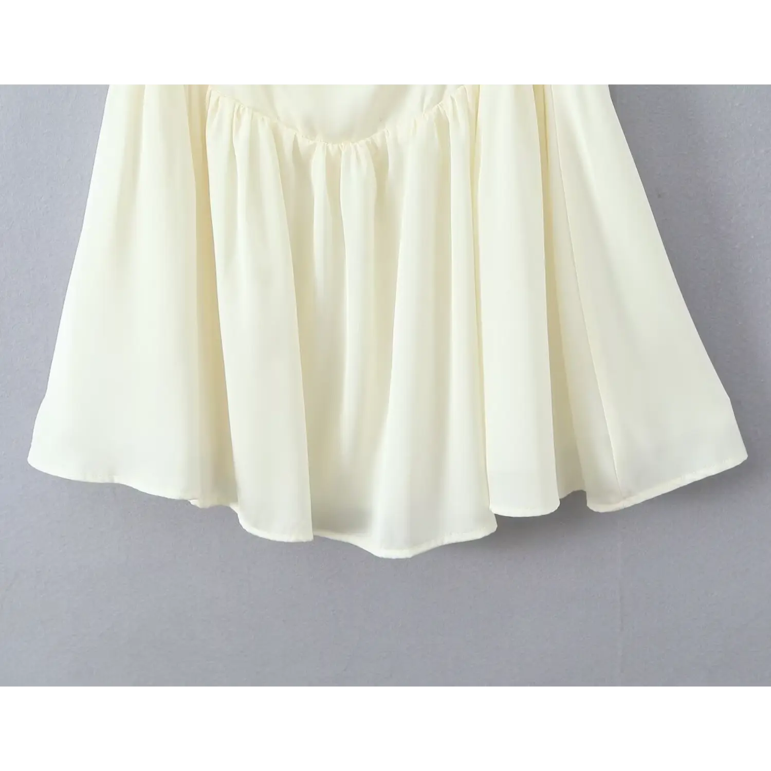 Close‑up gathered flared skirt hem lightweight flowy fabric cream cami mini dress grey wall background