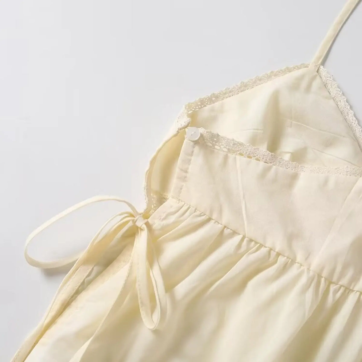 Detail shot of cream camisole side tie and decorative button, lace trim on v neckline