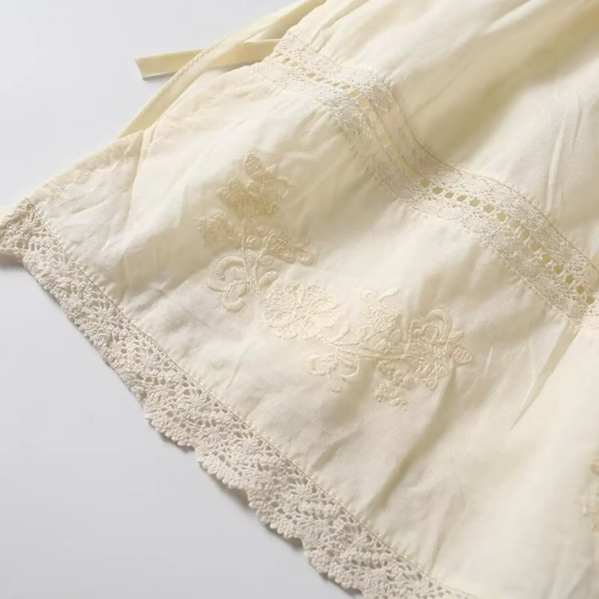 Macro closeup of cream camisole floral embroidery, vintage flower pattern with scalloped lace edge