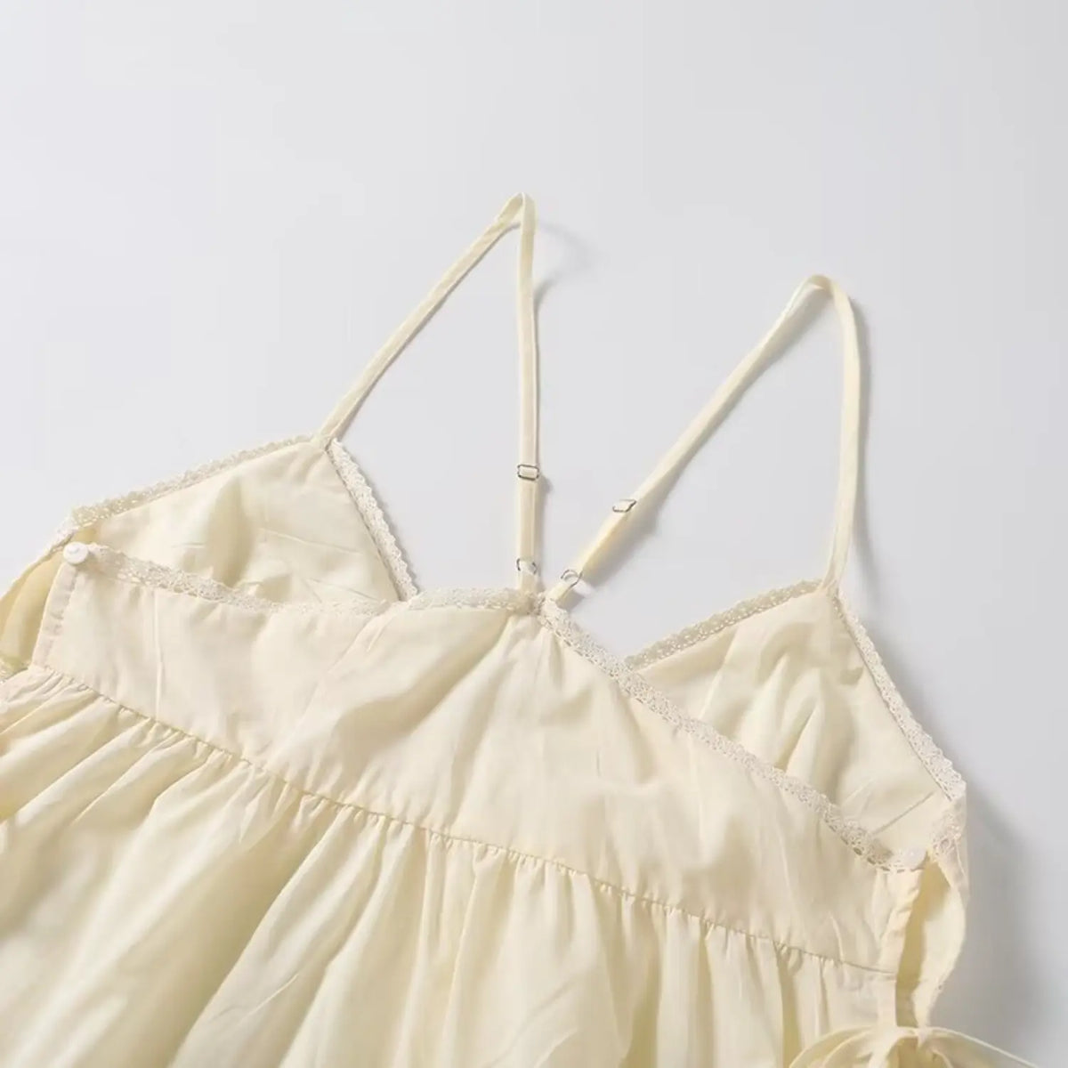 Cream lace cami top overhead view, v neckline, adjustable spaghetti cross straps and gathered bust
