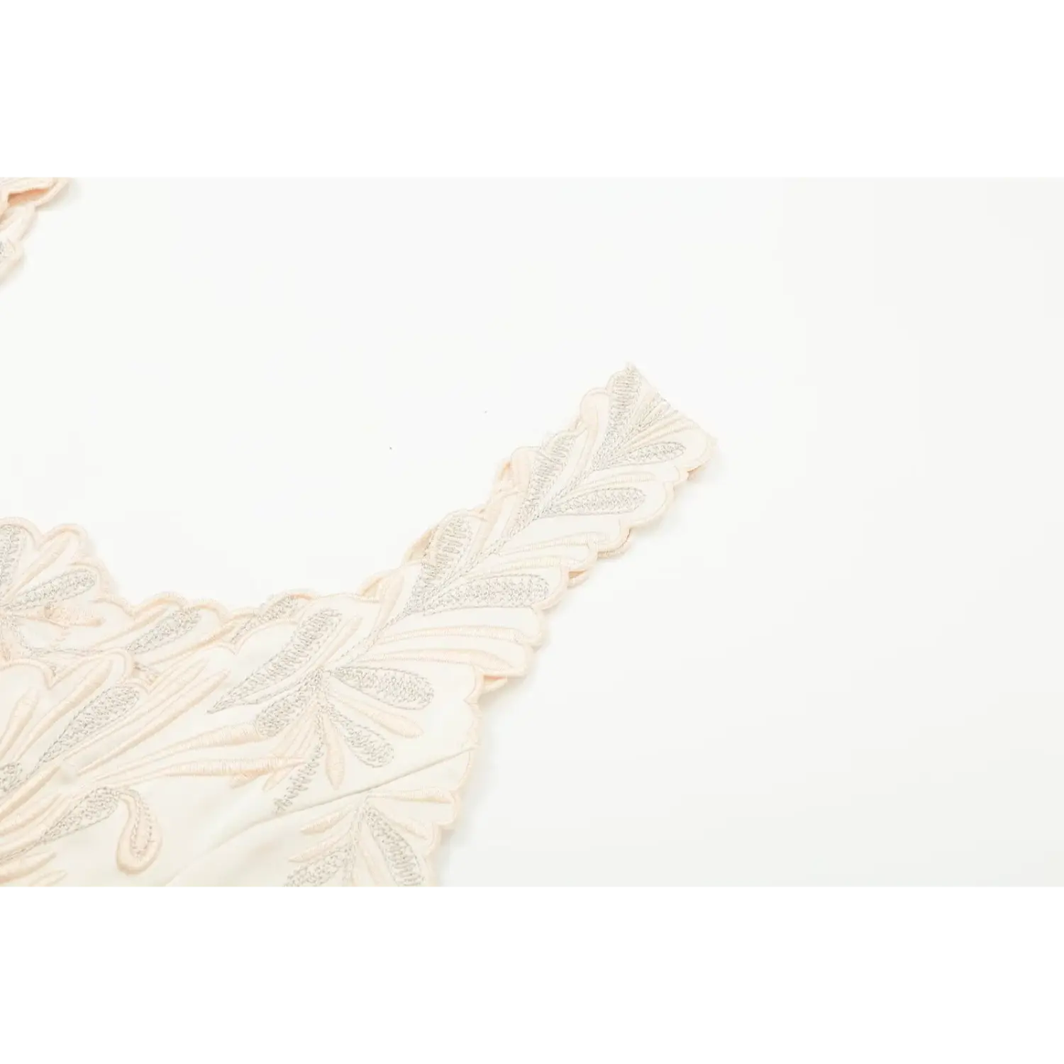 Detail shot of scalloped embroidered strap on cream floral camisole top