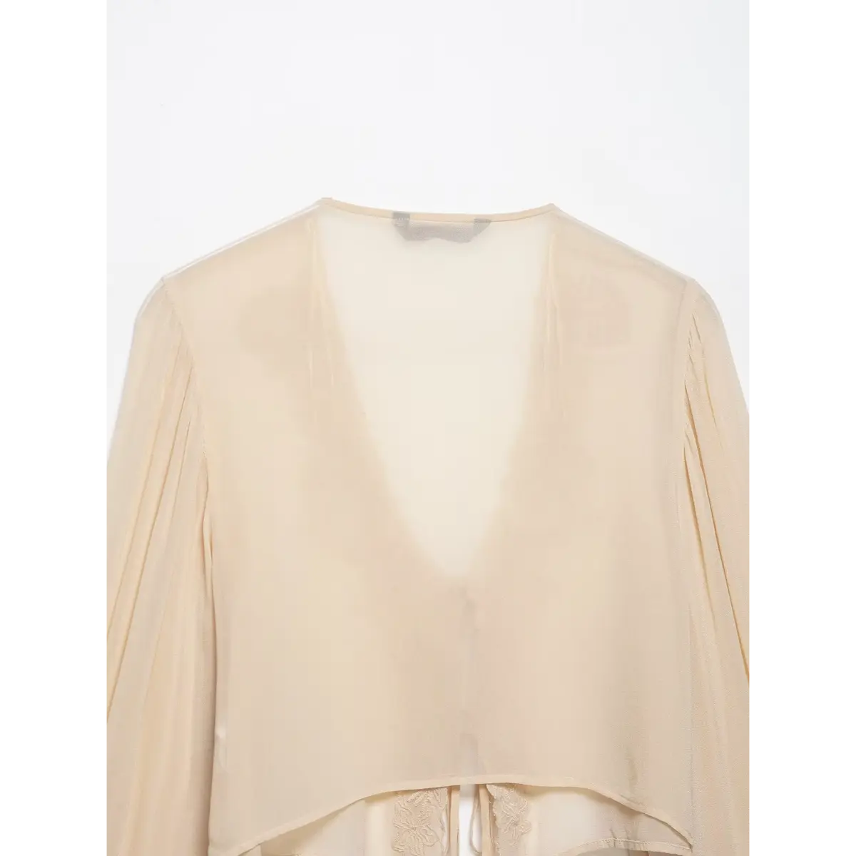 Bottom view of a cream chiffon blouse, showing both bell sleeves with drawstring cuffs and the cropped hem.