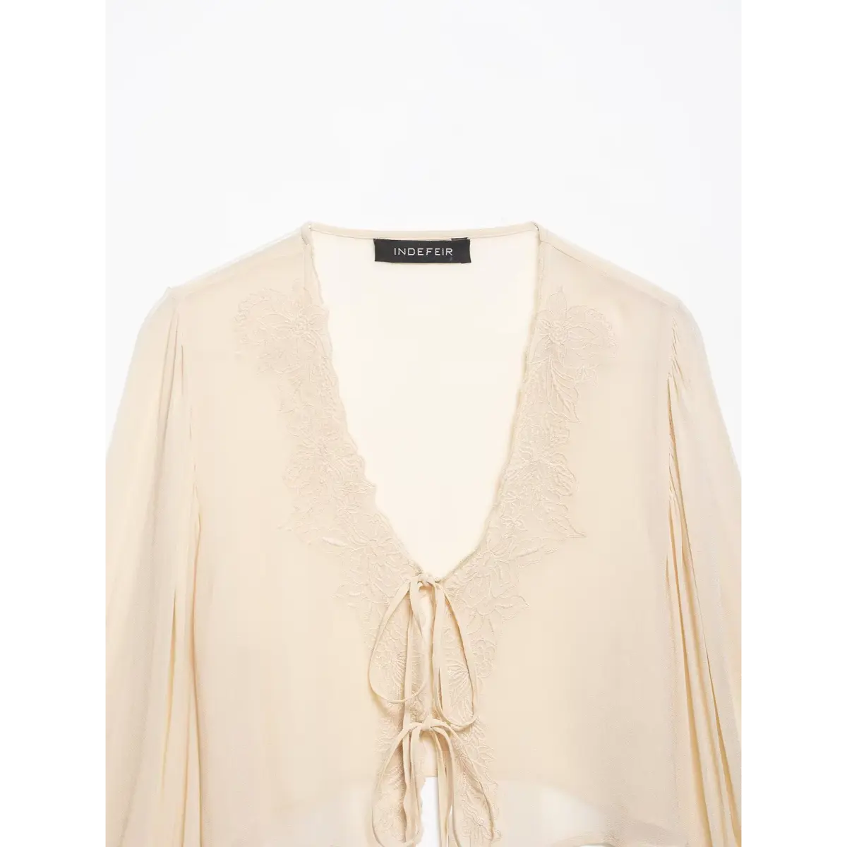 Close-up front view of a cream chiffon blouse with lace embroidery and tie-front detail, showing the neckline and label.