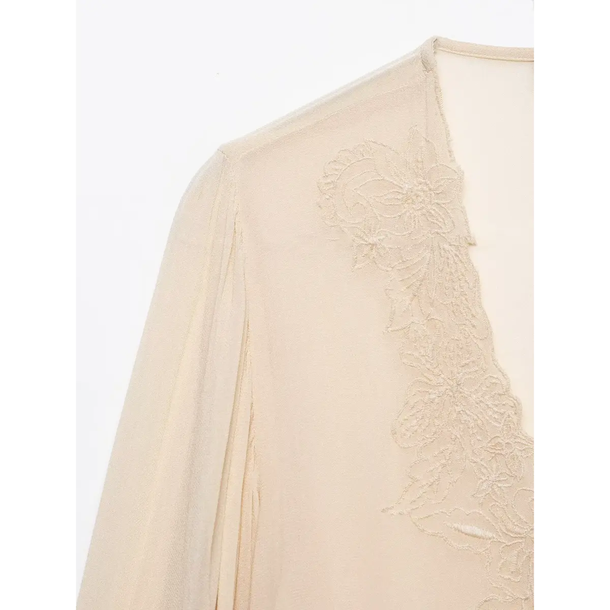 Close-up of the floral lace embroidery along the V-neckline of a cream chiffon blouse.