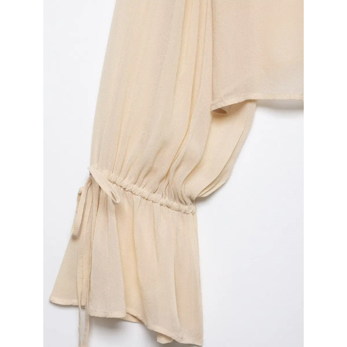 Close-up detail shot of the bell sleeve on a cream chiffon blouse, highlighting the gathered drawstring cuff and flowy fabric.