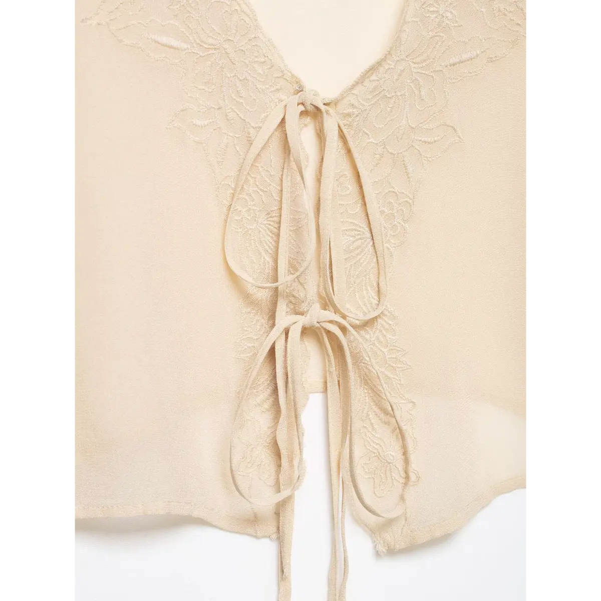 Close-up of the tie-front and lace embroidery on a cream chiffon blouse, highlighting the texture of the fabric ties and floral pattern.