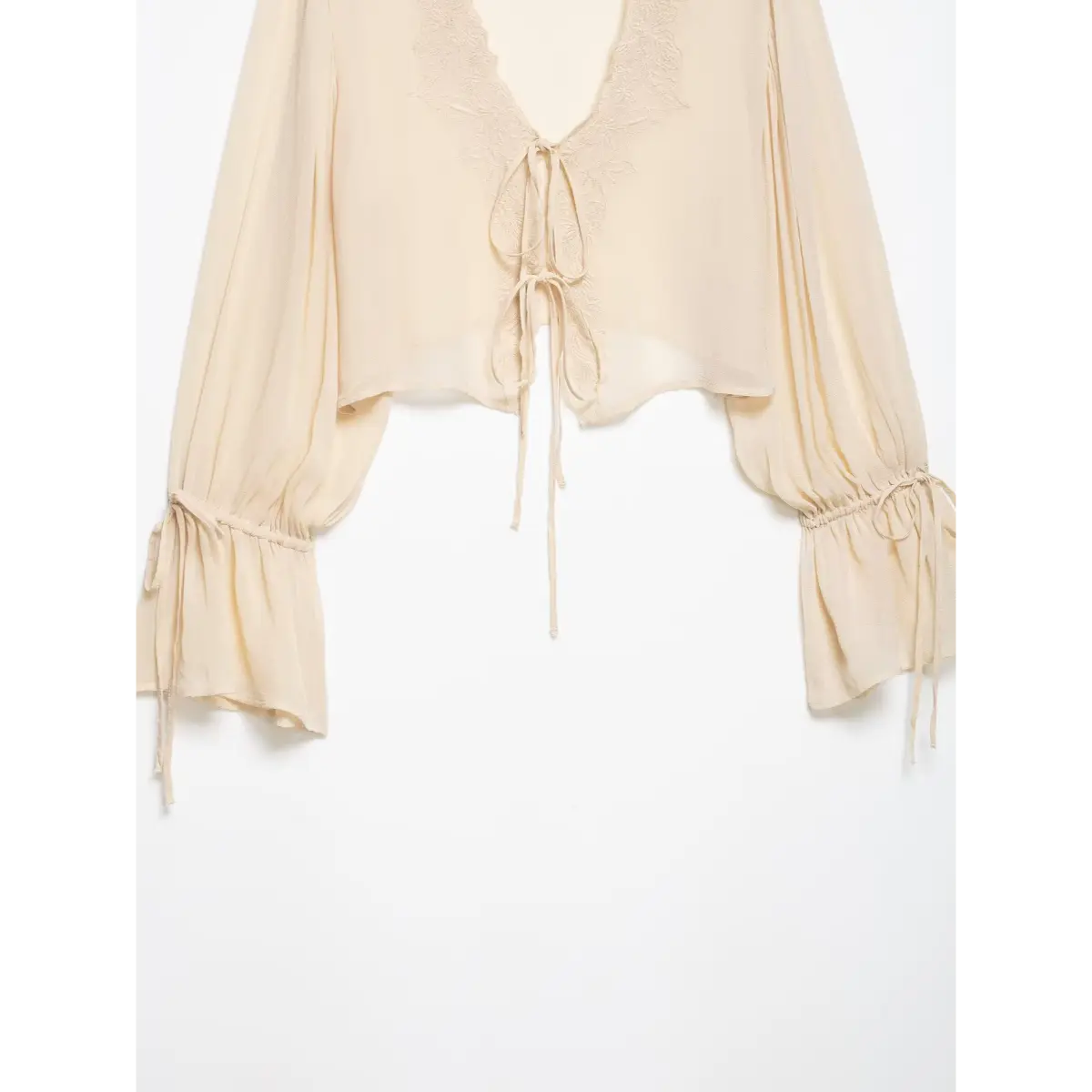 Close-up of the tie-front and lace embroidery on a cream chiffon blouse, highlighting the texture of the fabric ties and floral pattern.