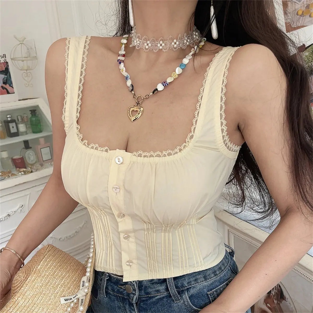 Front view of the cream lace-trimmed corset cami top, featuring a square neckline, lace trim, button placket, and pleated corset detailing