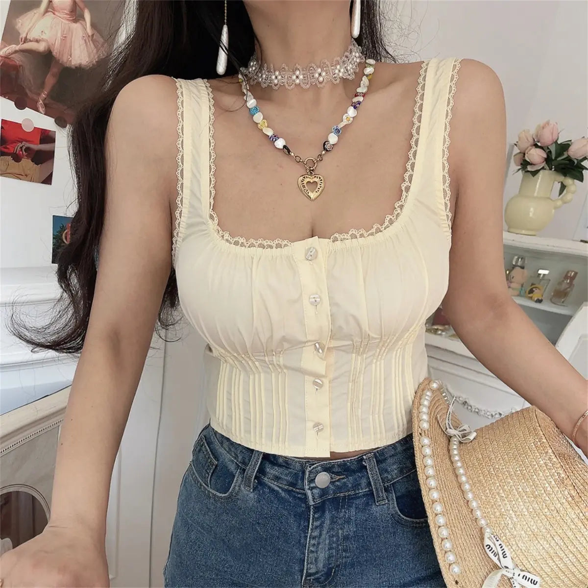 The cream lace-trimmed corset cami top styled with denim shorts and a pearl-trimmed straw hat