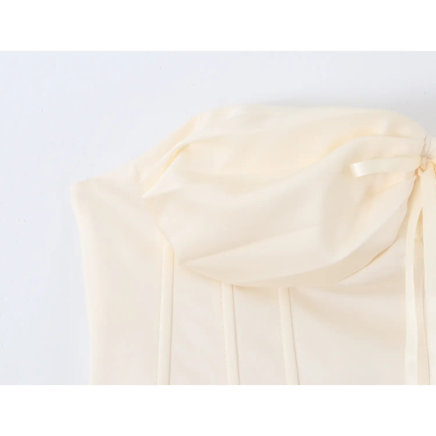 Side close‑up of oversized fabric bow on cream strapless corset top, smooth satin fabric texture