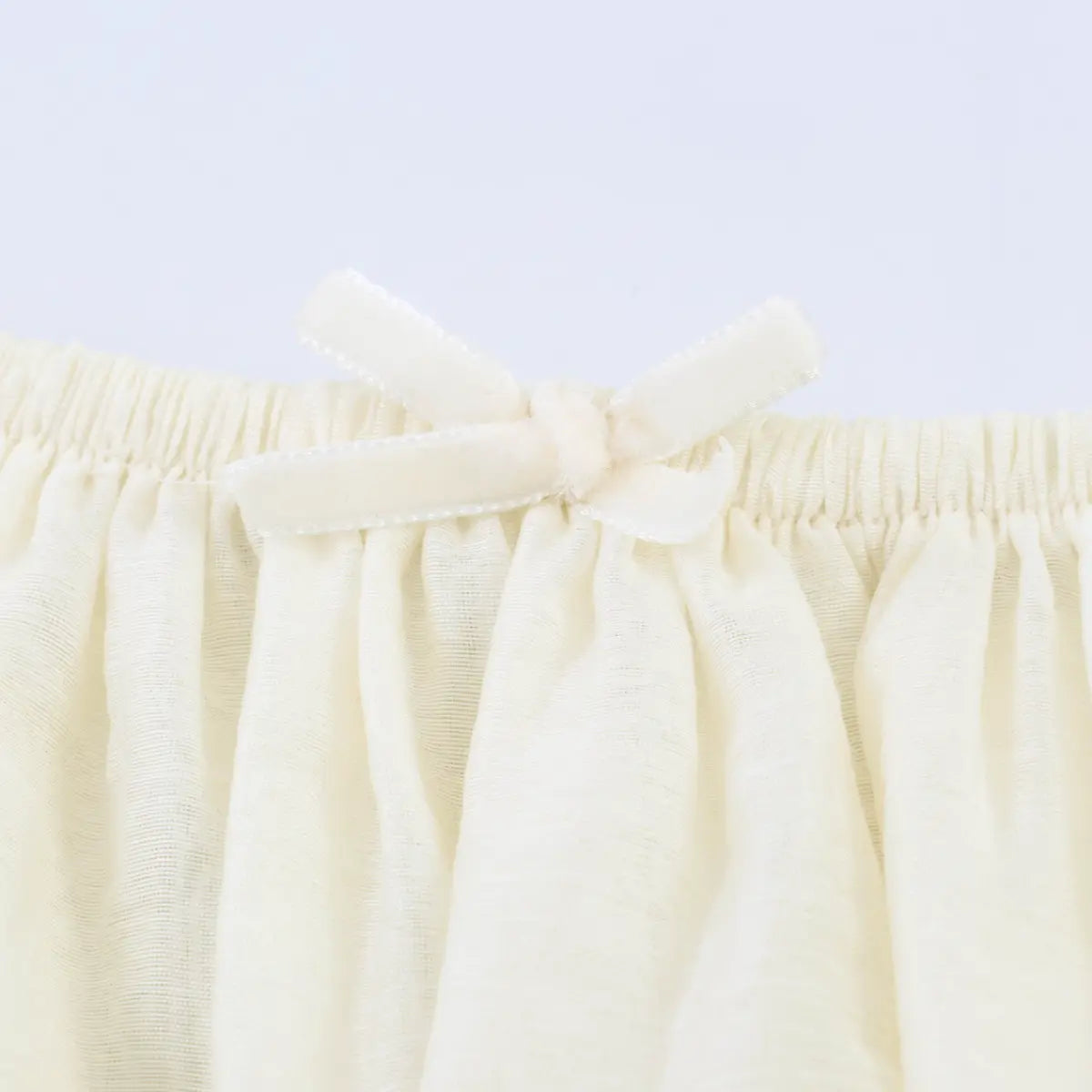 Close-up of the delicate ribbon bow at the center front neckline, above the gathered fabric.