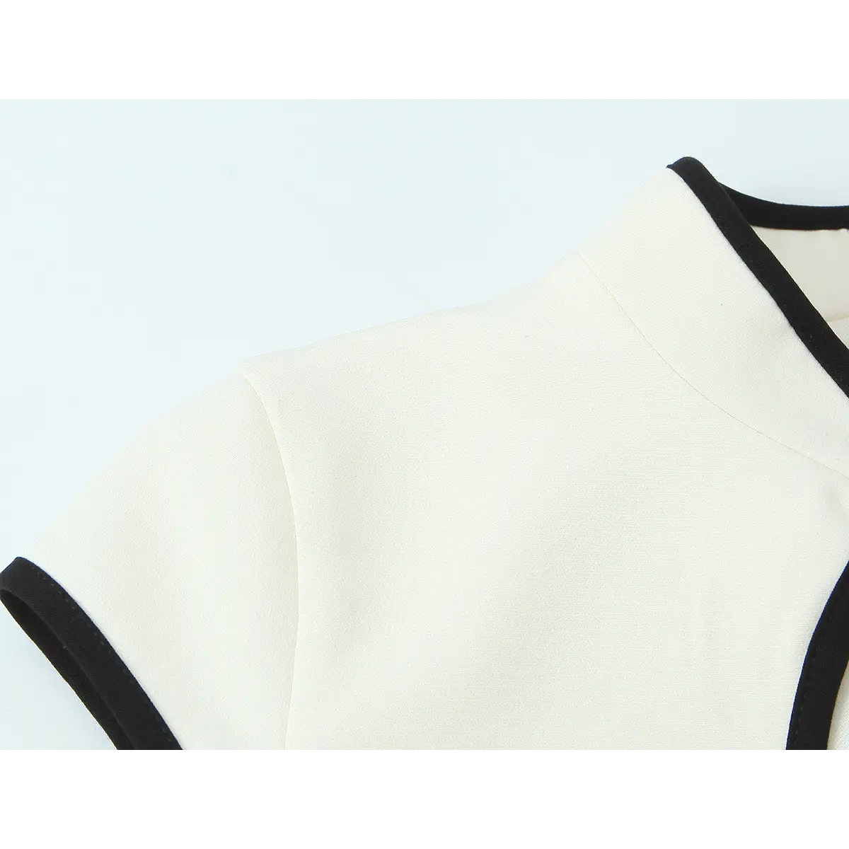 Close-up of the mandarin collar on the cream qipao dress, showing the clean black contrast piping and cap sleeve edge