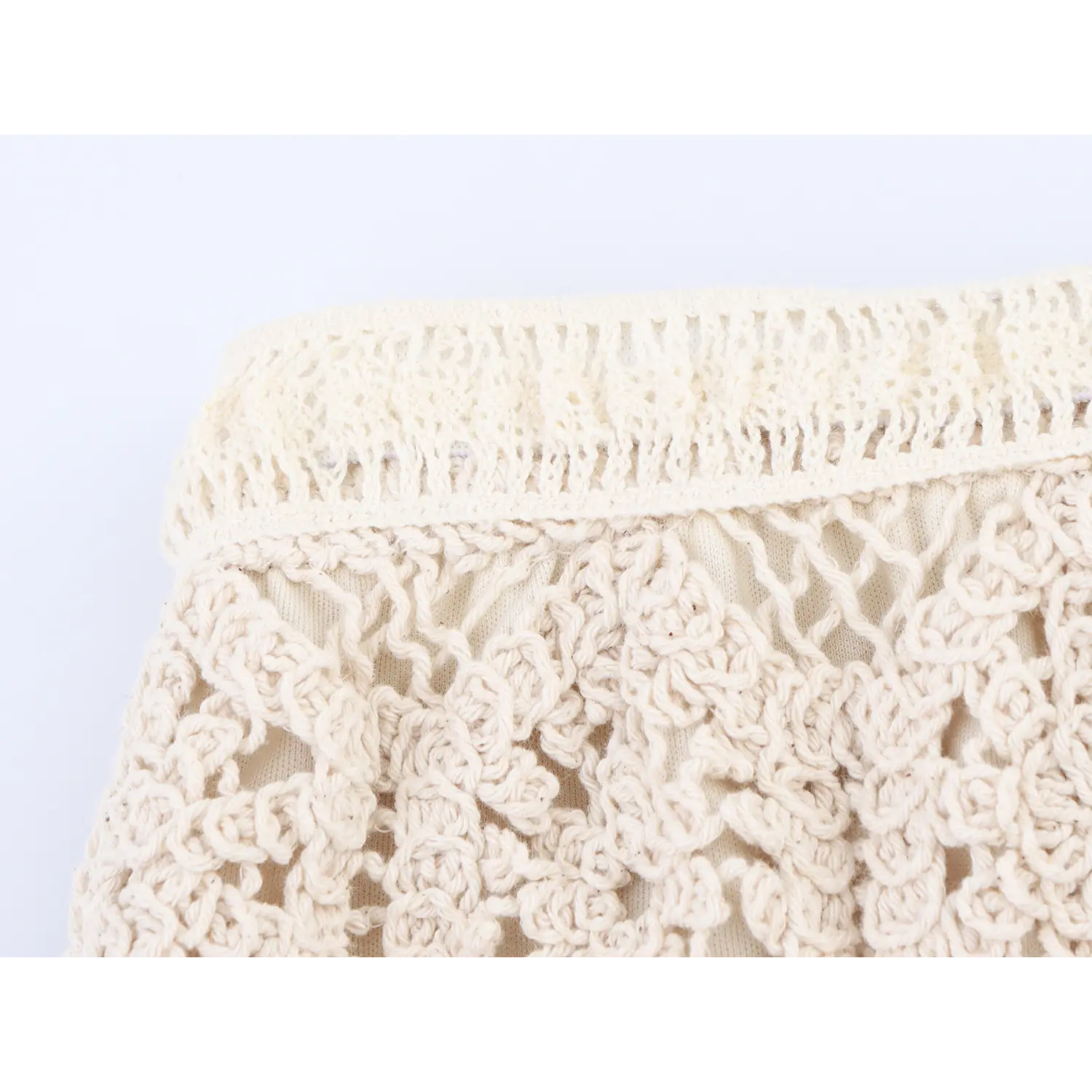 Close-up shot of elastic waistband and open crochet knit on cream boho skirt