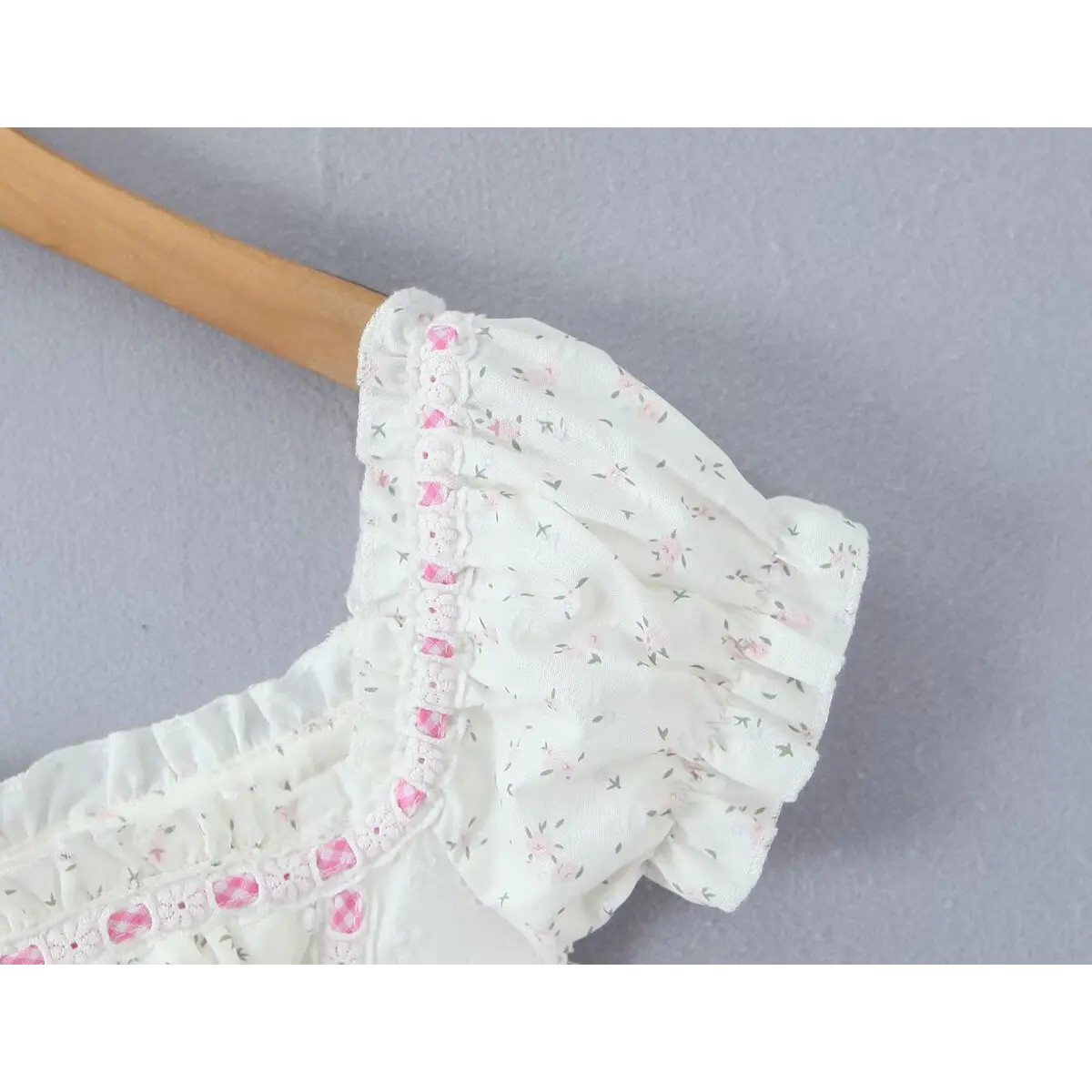 Close-up of the puffed short sleeve, showing the floral print, ruffled cuff, and pink checkered lace trim.