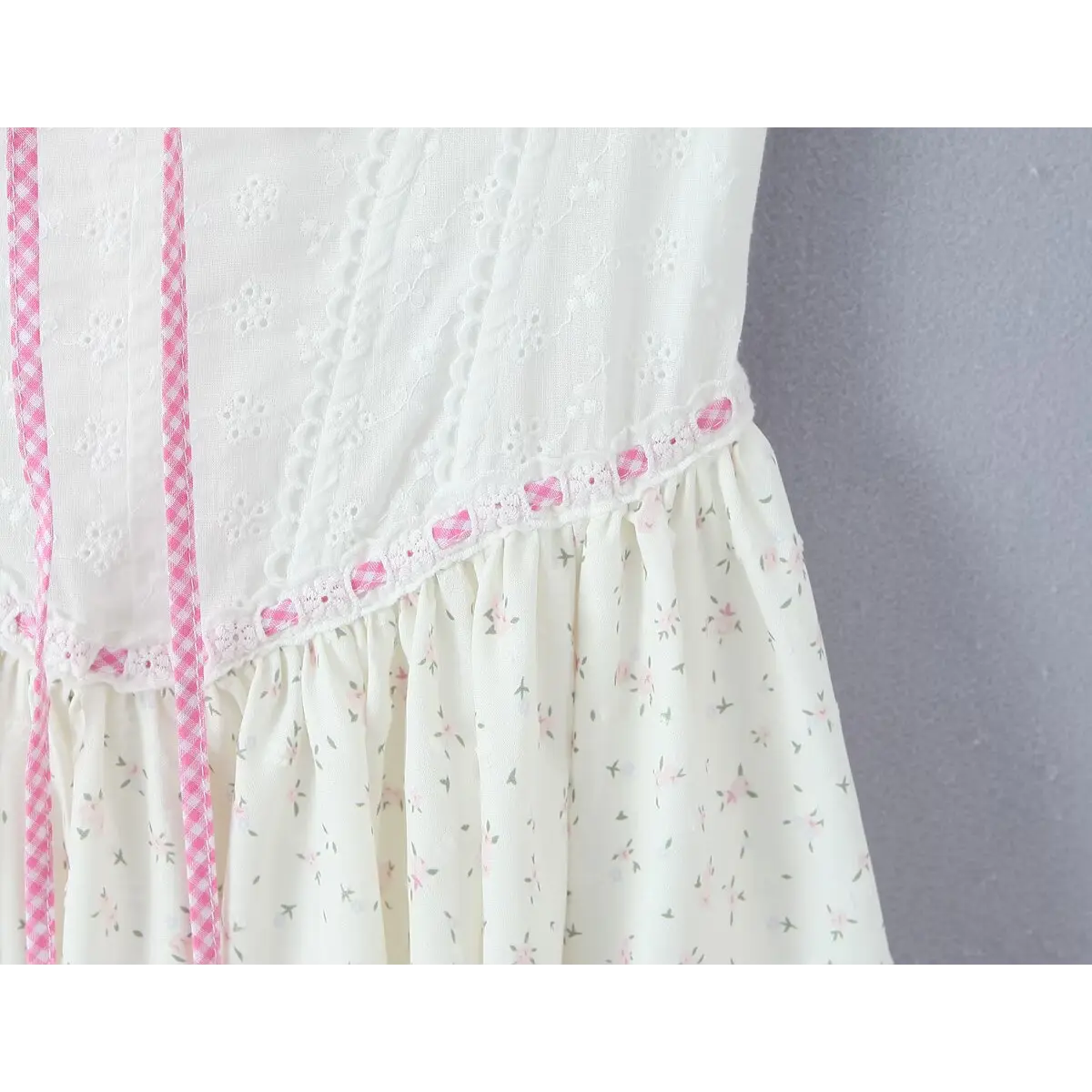 Close-up of the waist seam, showing the transition from the embroidered bodice to the gathered floral skirt with pink lace trim.