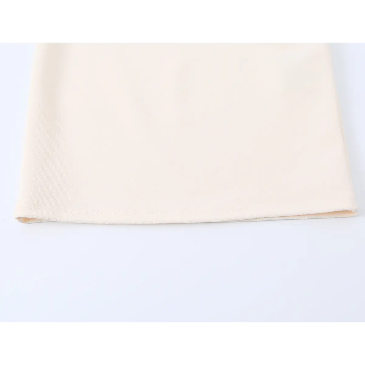 Close-up of the dress's straight hem, showing the neat stitching and soft cream fabric finish.