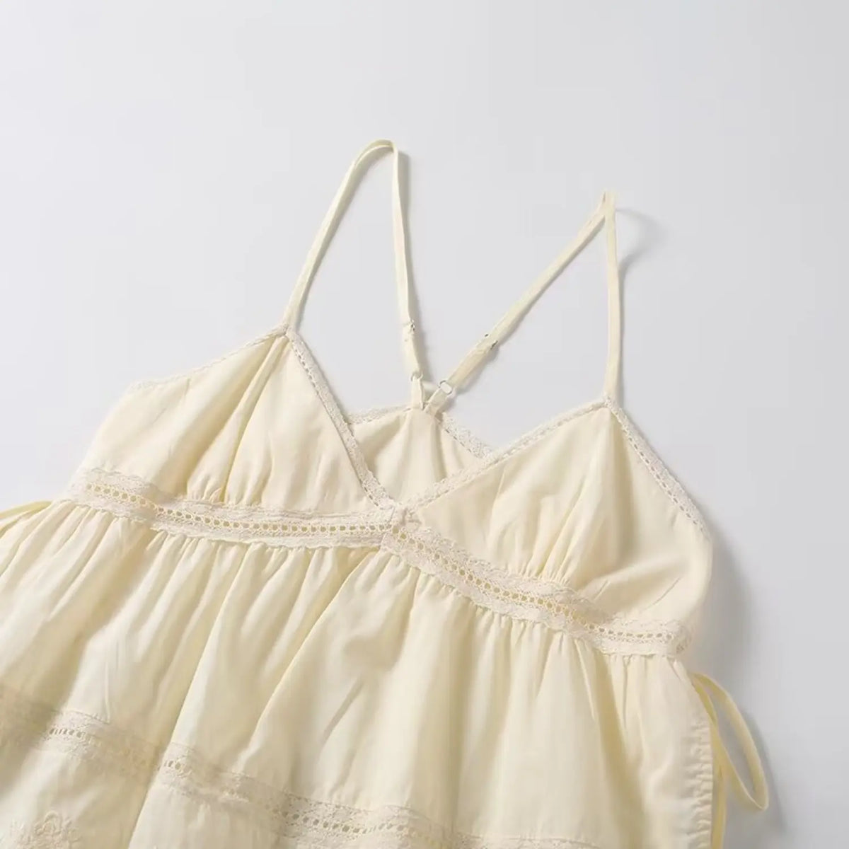 Angled shot of cream lace cami top, showing v neckline, eyelet lace panel and gathered babydoll silhouette