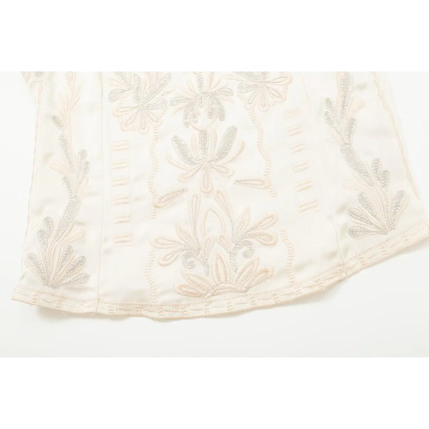Flat close‑up of embroidered hem and bottom floral motifs on cream camisole