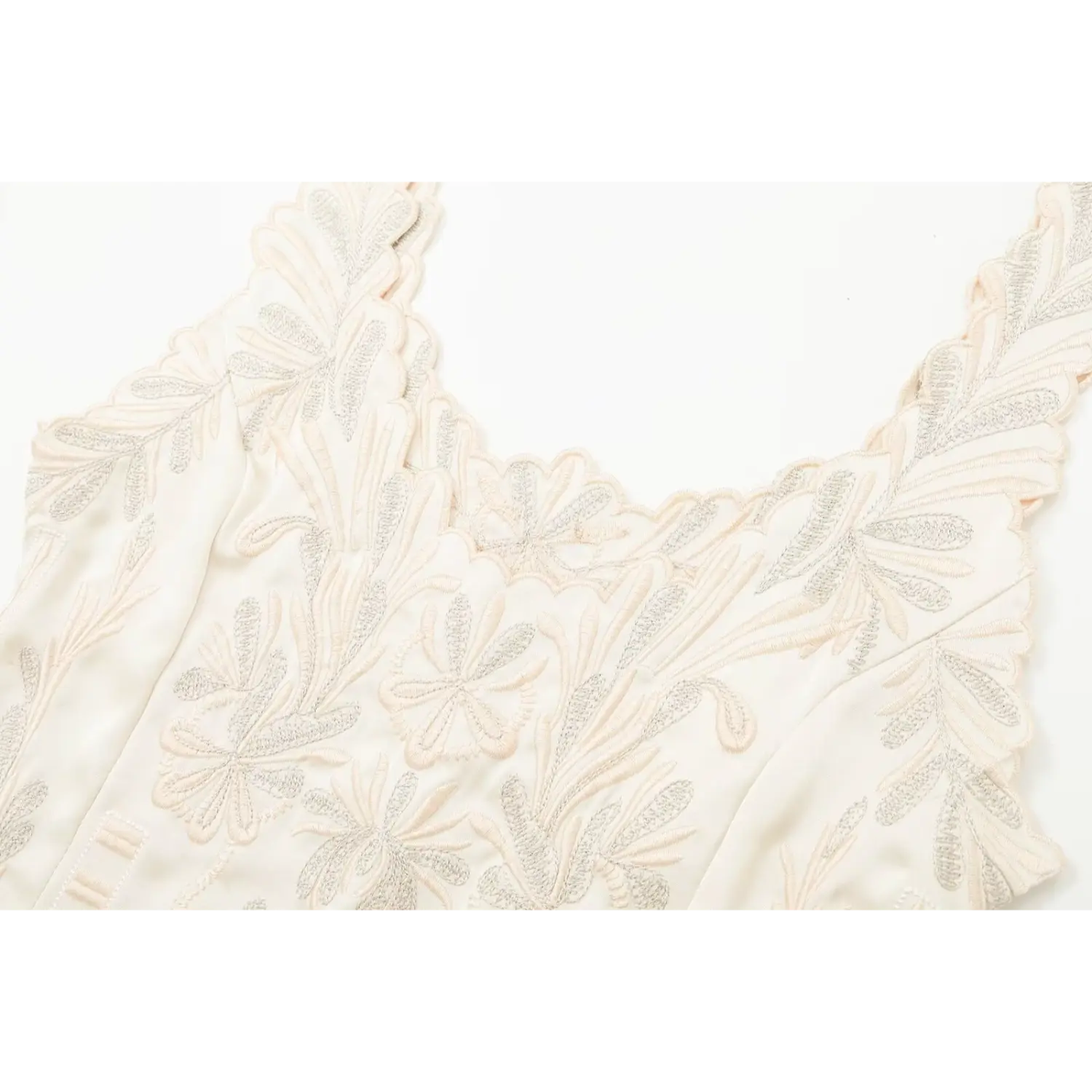 Close‑up of scalloped neckline and floral embroidery on cream satin camisole top