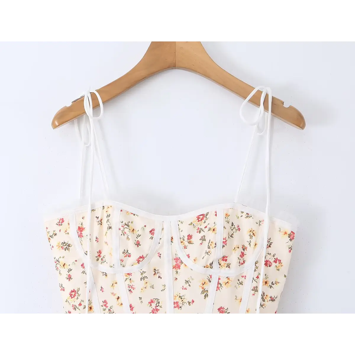 Cream floral print cami dress hanging on wooden hanger, showing thin tie straps and bodice