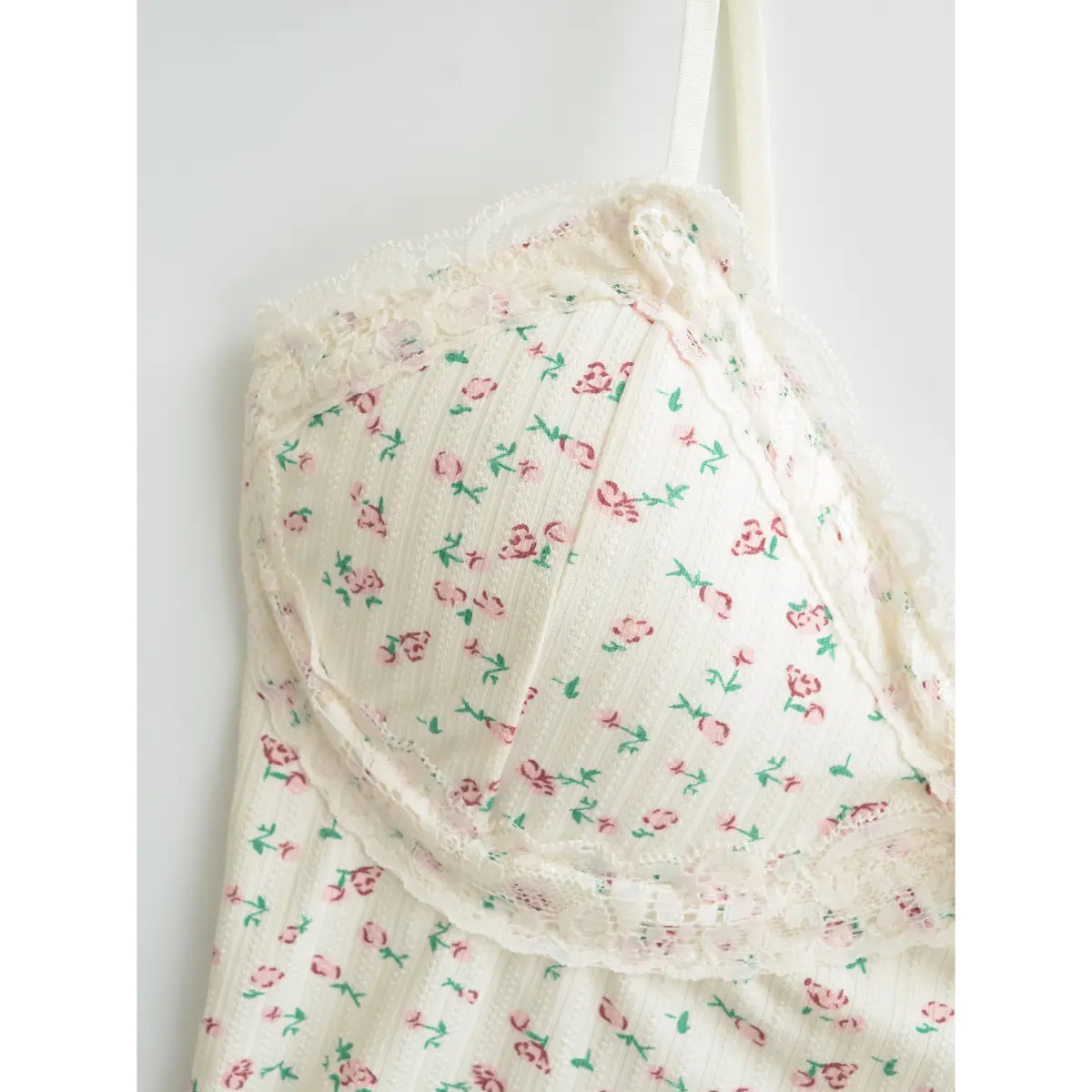 Close-up of the bust area on a cream floral cami top, highlighting the lace trim and fabric rose accent.