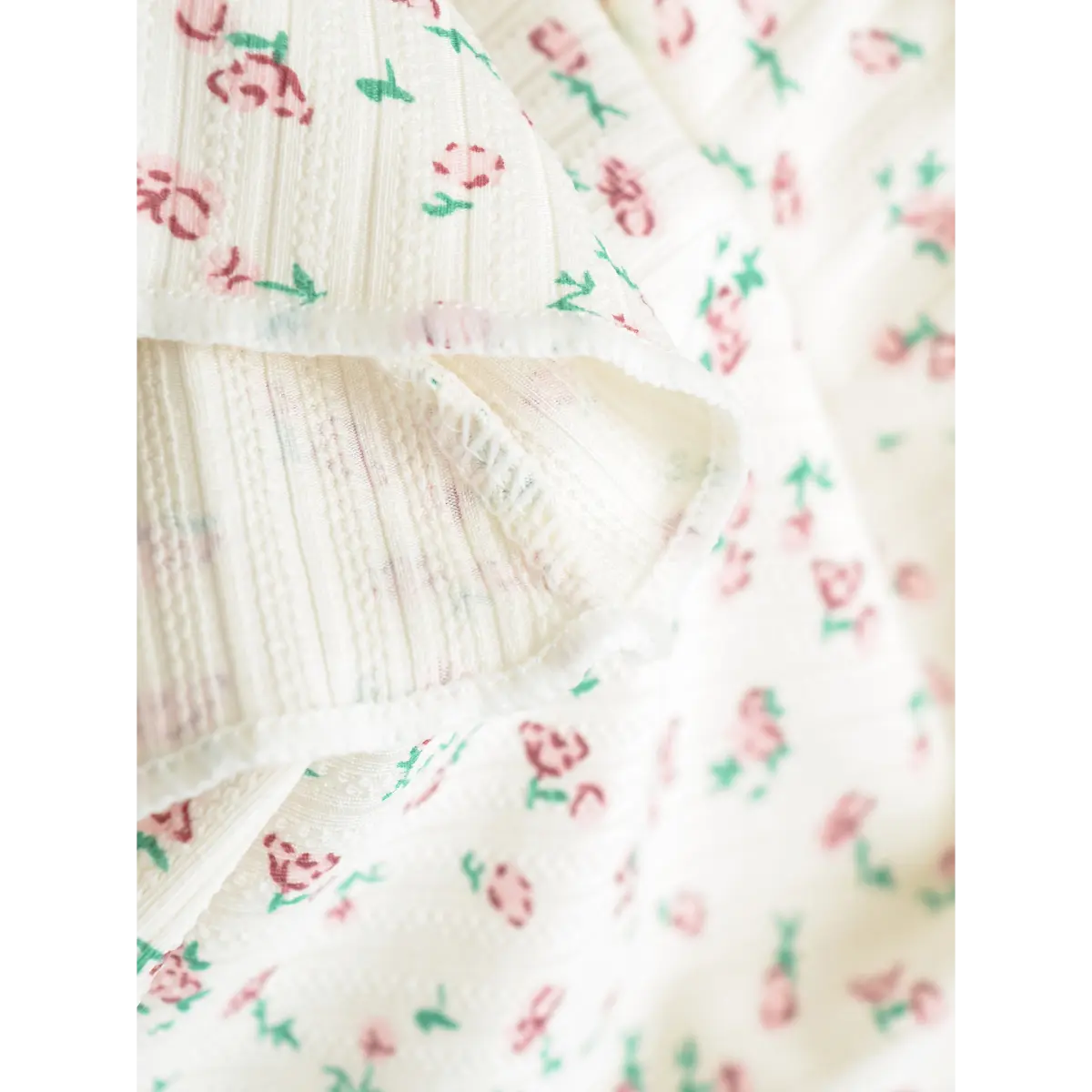 Close-up of the fabric texture on a cream floral cami top, highlighting the ribbed knit and pink rose print pattern.