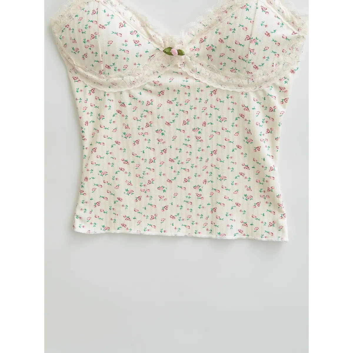 Flat-lay view of a cream floral cami top, displaying the full print, lace trim, and fabric rose accent.