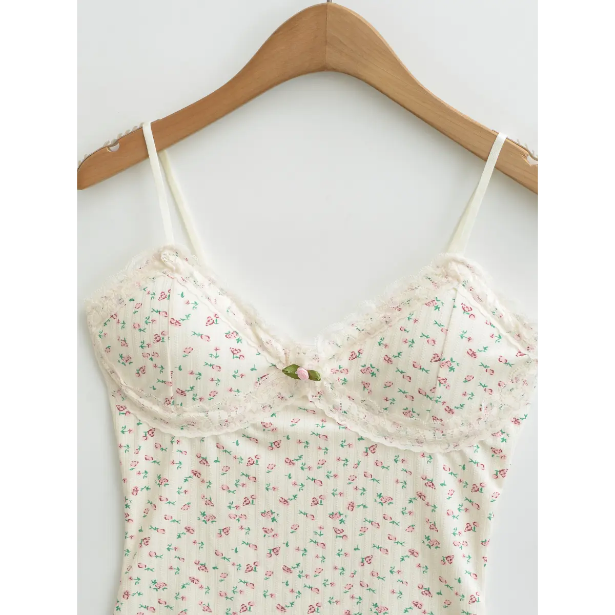 Full front view of a cream floral cami top hanging on a wooden hanger, showcasing the lace-trimmed bust and adjustable straps.