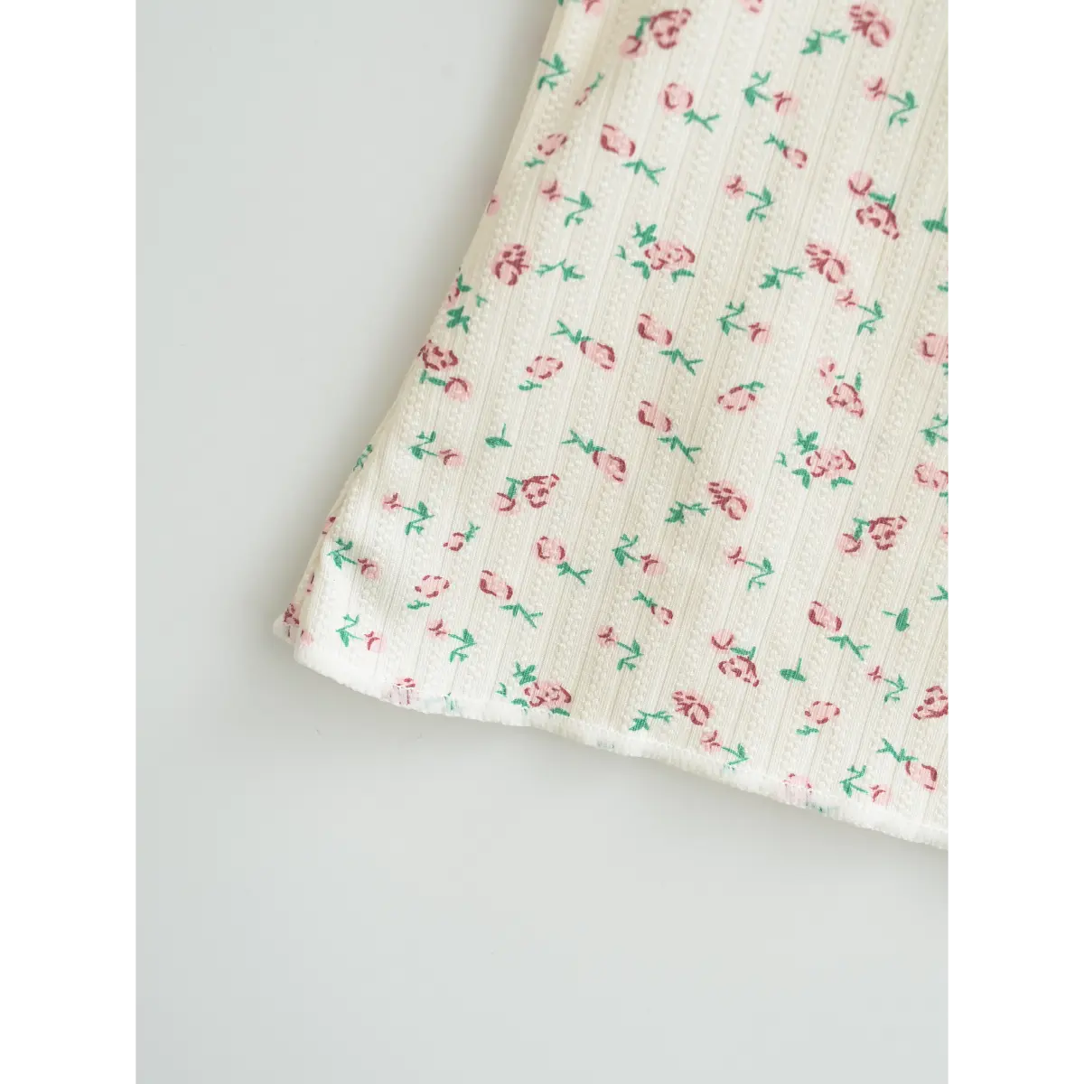 Close-up of the hem on a cream floral cami top, showing the ribbed fabric texture and delicate pink rose print.