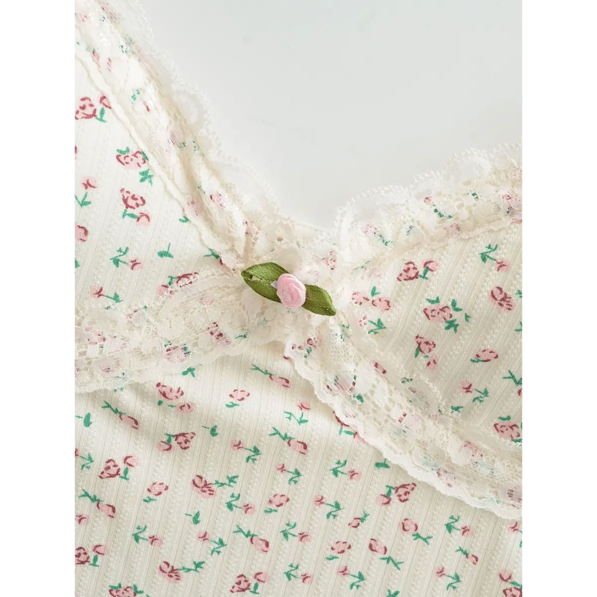 Close-up of the V-neckline on a cream floral cami top, featuring lace trim and a tiny fabric rose accent at the center.