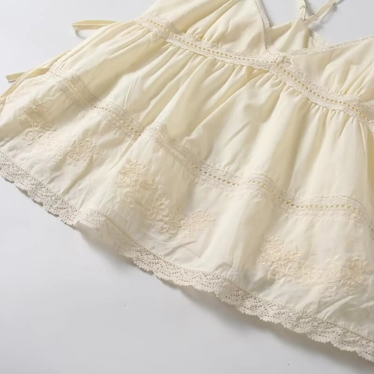Hem detail of cream cami top, floral embroidery and scalloped lace trim, tiered babydoll cut