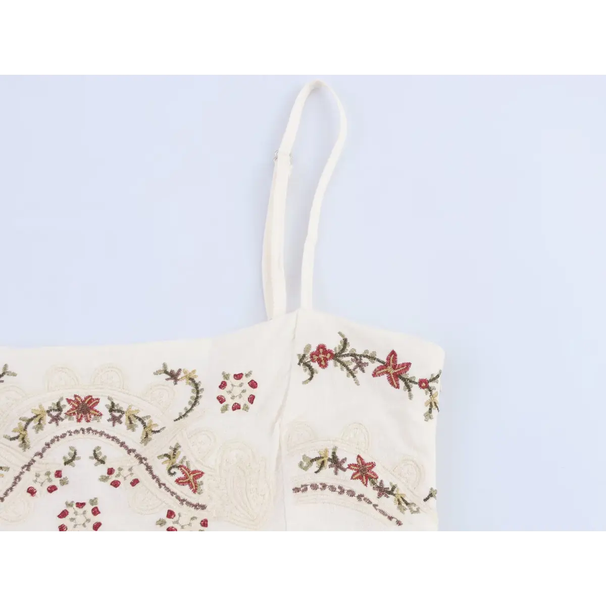  Close-up of the detailed embroidery on the bodice and adjustable strap of the cream dress.