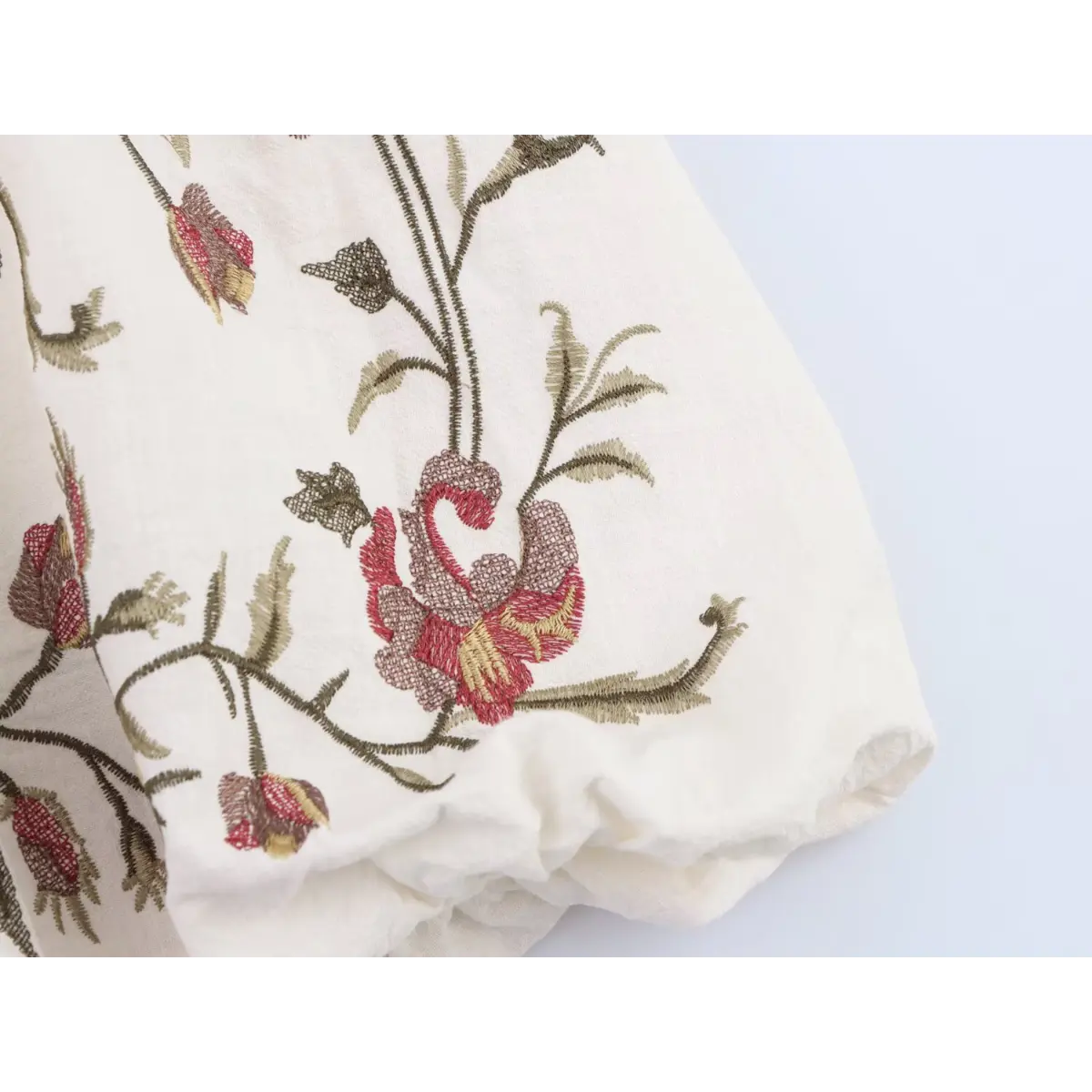 Close-up of the intricate floral embroidery on the skirt hem of the cream linen dress.