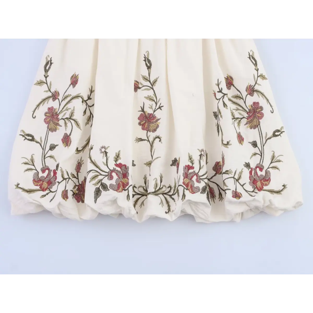 Full view of the gathered skirt hem with all-over floral embroidery on the cream dress.