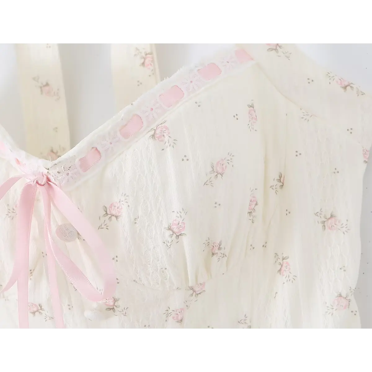 Close-up of the halter neckline, pink ribbon tie, and floral print on the cream dress