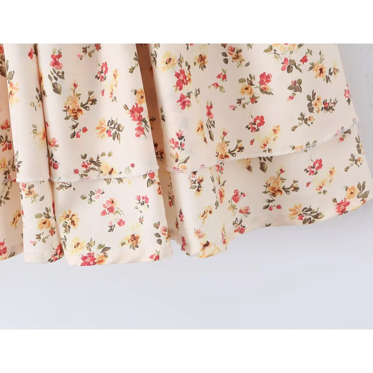 Close-up of the layered tiered skirt hem on the cream floral print cami dress