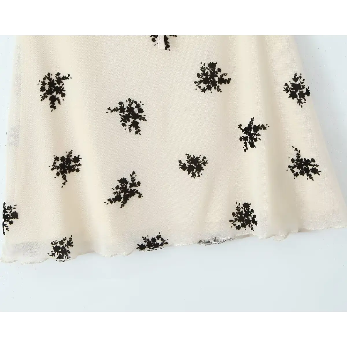 View of the flared skirt hem, showcasing the scalloped edge and all-over black floral pattern.