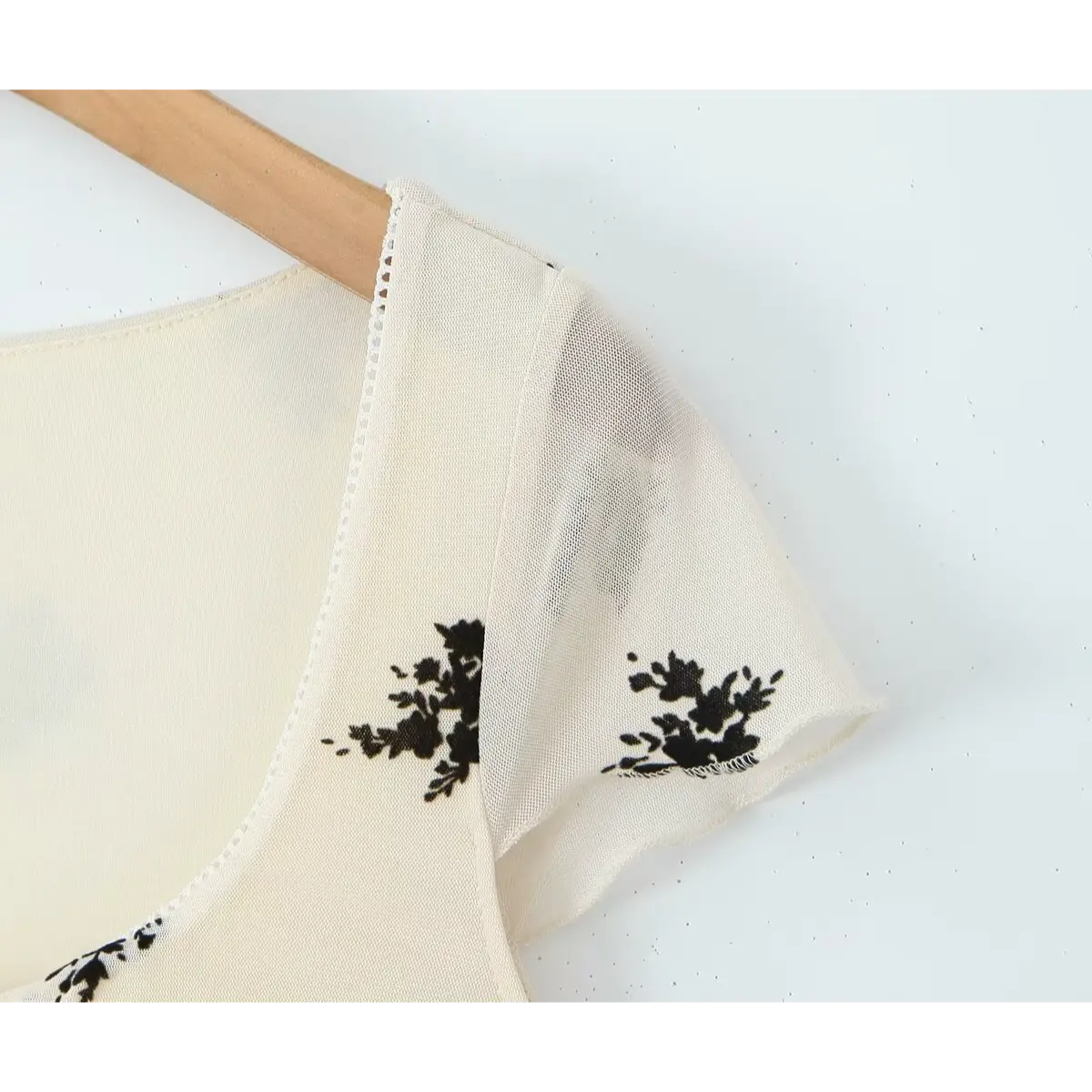 Close-up of the short cap sleeve, featuring the sheer mesh fabric and black floral print.